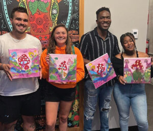 Two couples attending a date night paint and sip at Artvana holding their paintings and smiling