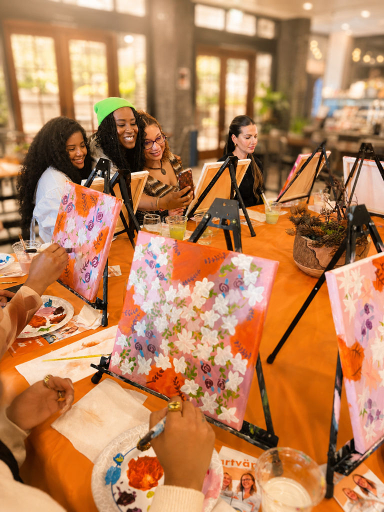 women laughing and raising a glass to cheers at a paint party for a girls night celebration