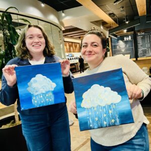 two friends holding up their finished paintings after a paint and sip class in gig harbor WA