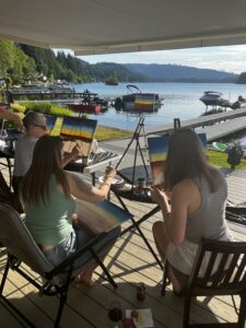 women painitng on a patio facing the water in summer hosting an artvana paint and sip private party